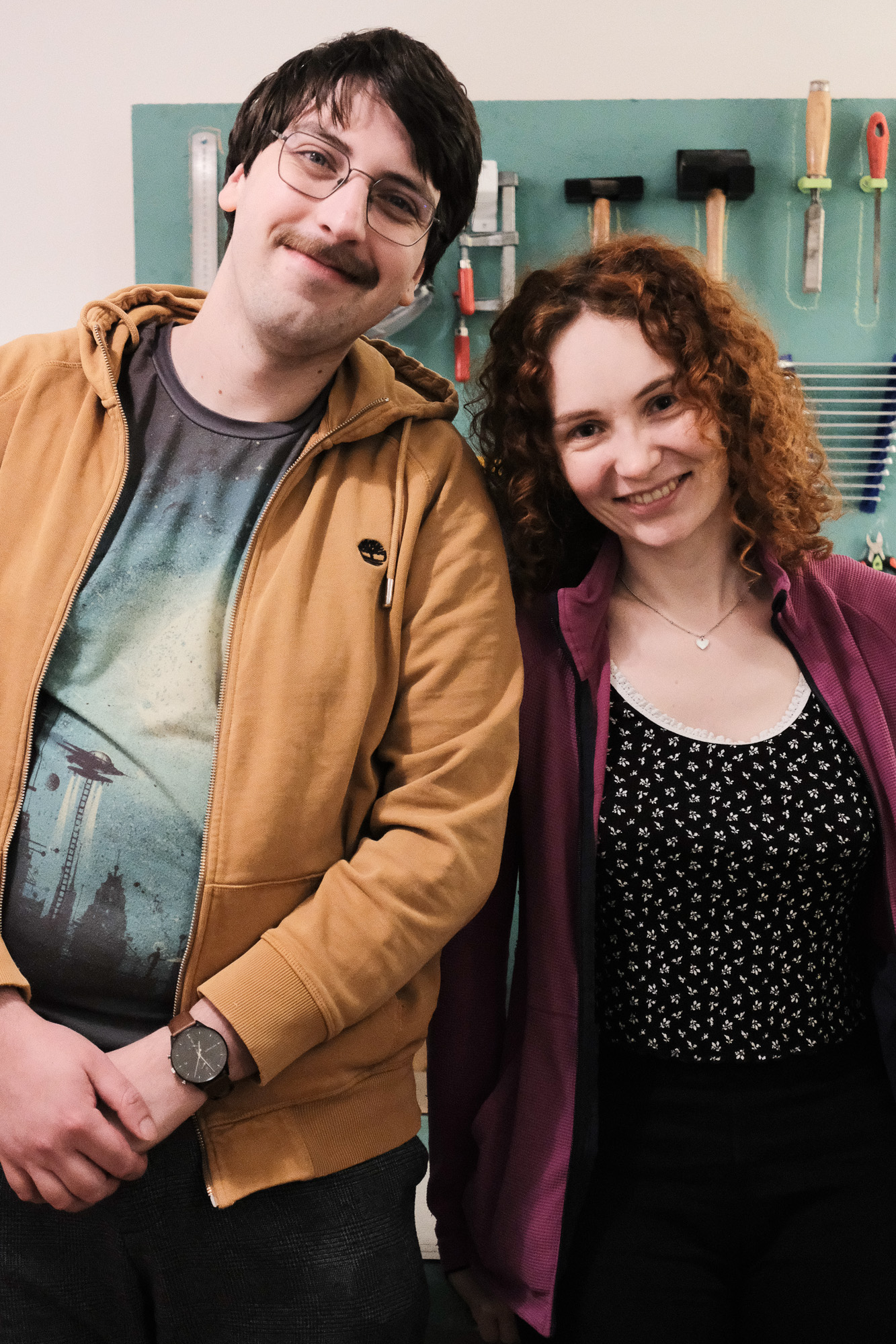 Two people (jupfi, ogalbnafets) standing next to each other smiling at the camera. Some tools (hammers, wrenches, ...) can be seen in the background.